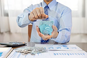 Businessman hand putting coin into blue piggy bank, saving money for future investment plan and retirement fund concept