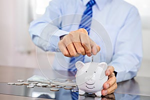 Businessman hand putting coin into blue piggy bank, saving money for future investment plan and retirement fund concept