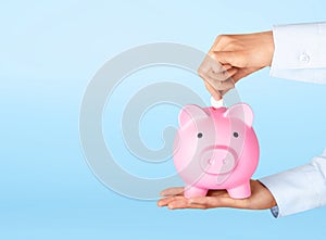 Businessman hand putting coin in piggy bank. Money saving, finance, investment concept