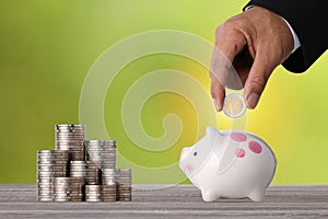 Businessman hand putting coin into piggy bank with saving growth on stacking coin growing, meaning of earning money or investment