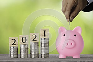 Businessman hand putting coin into piggy bank with saving growth year 2021 on stacking coin growing, meaning of earning money or