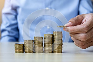 Businessman hand putting golden coin on growing money stairs or stack on wooden table. business, investment, retirement planning,