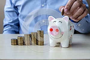 Businessman hand putting golden coin on piggy banking with growing money stairs or stack on wooden table. business, investment,