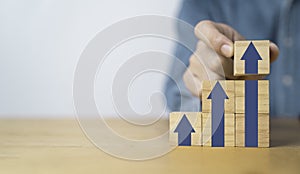 Businessman hand stacking up arrow on wooden block cube for economy interest rating growth and dividend profit from investment