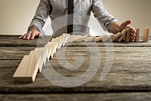 Businessman hand stopping domino effect