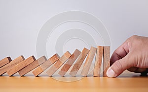 Businessman hand stopping falling blocks on table, stopping the domino effect concept for business solution, strategy and