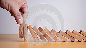 Businessman hand stopping falling blocks on table, stopping the domino effect concept for business solution, strategy and