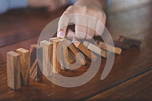 Businessman hand stopping falling wooden dominoes effect from continuous toppled or risk, strategy and successful intervention