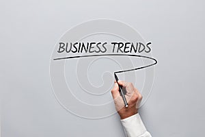 Businessman hand underlining the word business trends on gray background. Following business trends for success and creativity