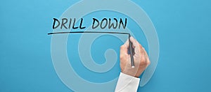 Businessman hand writing the business buzzword drill down on blue background. Going deep into the specific details of the