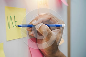 Businessman hand writing with colored sheets sticky note paper on white board background