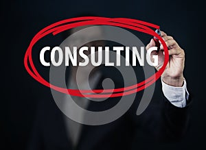 Businessman hand writing `Consulting` with red marker on transparent board.