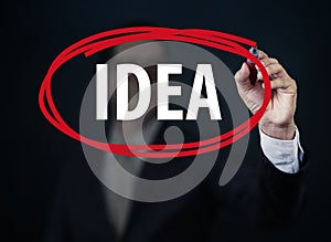 Businessman hand writing `IDEA` with red marker on transparent board.