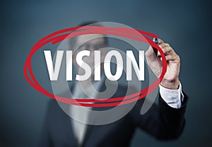 Businessman hand writing `VISION` with red marker on transparent board.