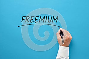 Businessman hand writing the word freemium on blue background. Using free content to attract new customers in business