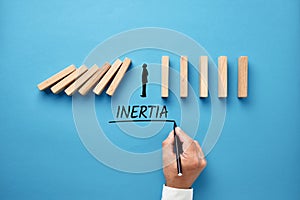 Businessman hand writing the word inertia with silhouette of a man standing against collapsing wooden dominos. Business inaction,