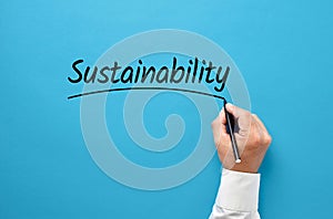 Businessman hand writing the word sustainability on blue background. Corporate environmental ecology strategy in business