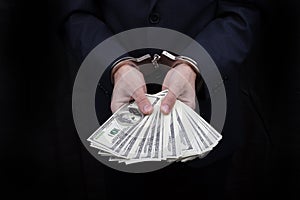 Businessman in handcuffs holding bribe many hundreds dollars