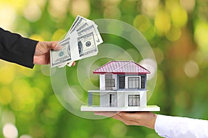 Businessman handed the money to Businesswoman holding model house on natural green background, New home and Real estate trading