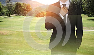 Businessman handles necktie showing confidence in golf course.