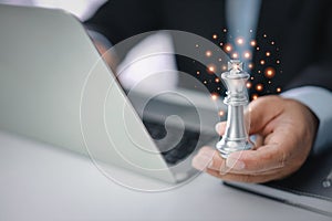 Businessman hands in black suite sitting and holding chess king on vintage table with computer on table meaning of planning and