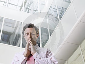 Businessman With Hands Clasped In Office Atrium