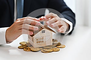Businessman hands protecting house model and pile of gold coins. Real estate, property investment and save money concept