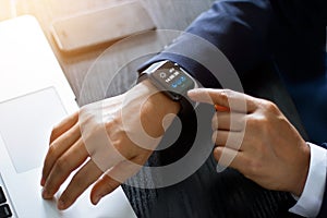 Businessman hands using smart watch app over laptop and smartphone on working desk, technology and communication concept. All on s