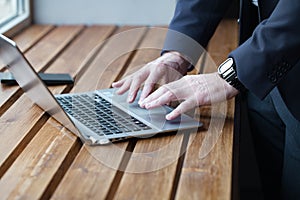 Businessman hands with watch are typing on keyboard, working on laptop. Close up on the wooden table
