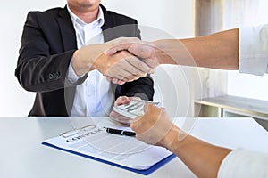 Businessman handshake with money of dollar banknotes in hands from money of their partner to give success the deal contract in a