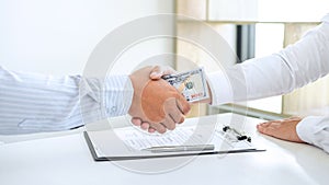 Businessman handshake with money of dollar banknotes in hands from money of their partner to give success the deal contract in a