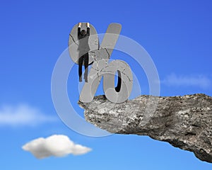 Businessman hanging on cracked percentage sign with cliff sky