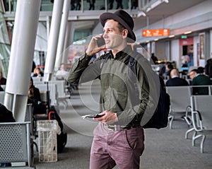 Businessman in a hat standing at the airport,talking by cellphone .