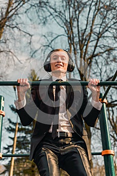 Businessman in headphones pulls himself up on a sports horizontal bar. Modern young man. Startup business concept.