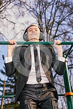 Businessman in headphones pulls himself up on a sports horizontal bar. modern young man. Startup business concept
