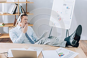 Businessman in headphones yawning while doing