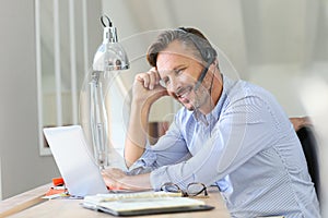 Businessman with headset teleworking on laptop