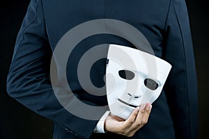 Businessman hide the white mask in the hand behind his back on b