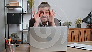 Businessman hiding behind laptop computer, making funny face, fooling around, putting his tongue out