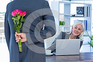 Businessman hiding flowers behind back for colleague