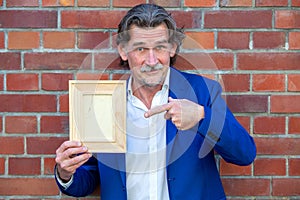 Businessman in his 50s in blue suit holding a wooden frame