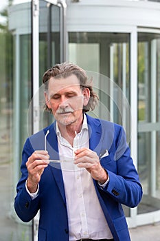 Businessman in his 50s standing outside holding his glasses