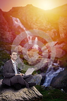 Businessman with his laptop sitting in a beautiful mountain scenery