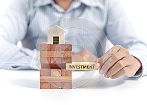 Businessman hold word investment on puzzle with wooden home model