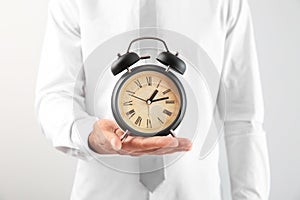 Businessman holding alarm clock on light background, closeup. Time management concept