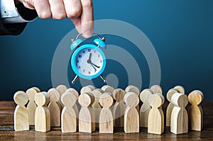 A businessman is holding an alarm clock over a crowd of people. Time management. Hourly wages, strict work limits and time