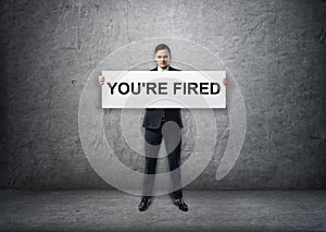 Businessman holding banner with 'you're fired' text on it in his hands