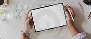 Businessman holding blank screen tablet above computer keyboard and supplies on white office desk