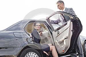 Businessman holding car door for colleague against sky