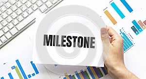 Businessman holding a card with text MILESTONE. Keyboard, diagram and white background